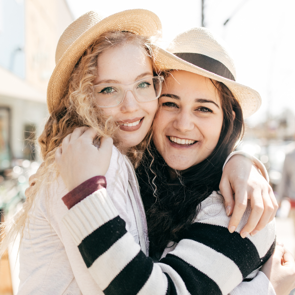Two girl friends with hats smiling at the camera while embracing