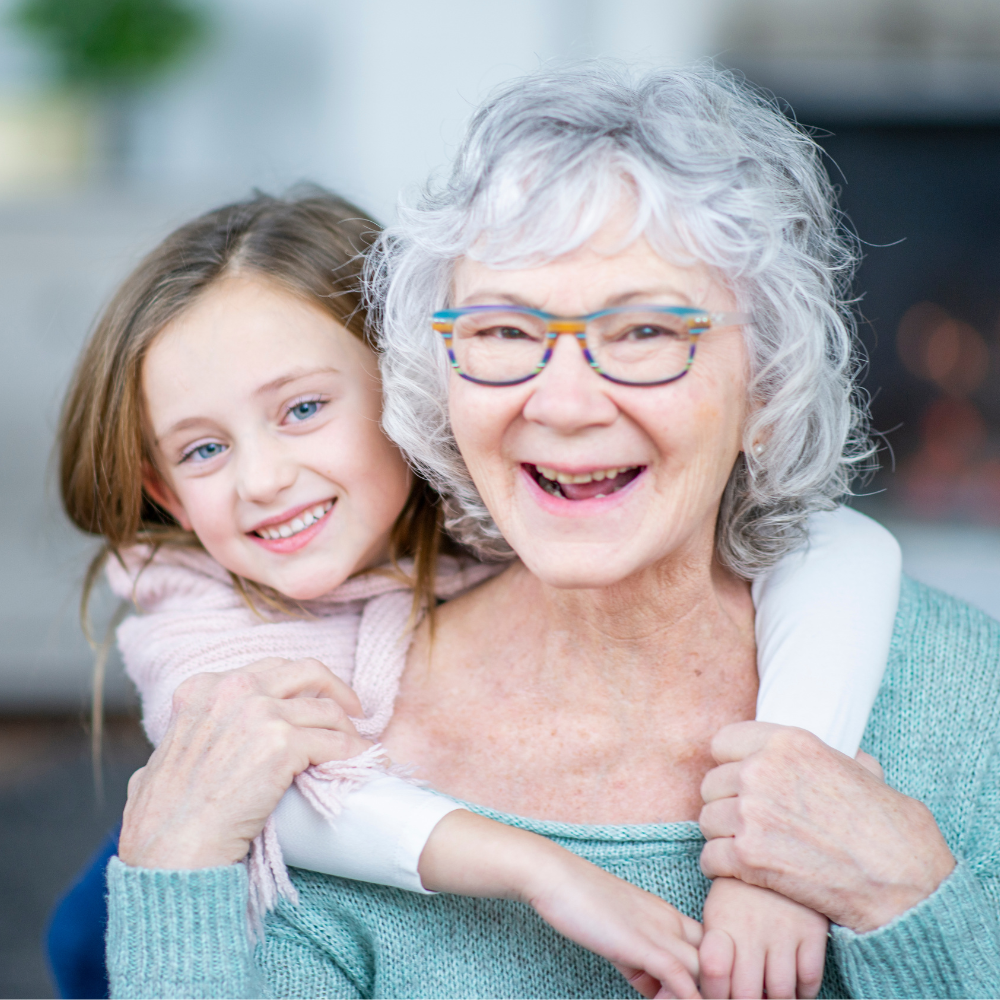 a grandma smiling with her granddaughter who is holding her arms around her neck