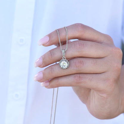 A diamond halo white gold necklace shown close up held in a woman's hand