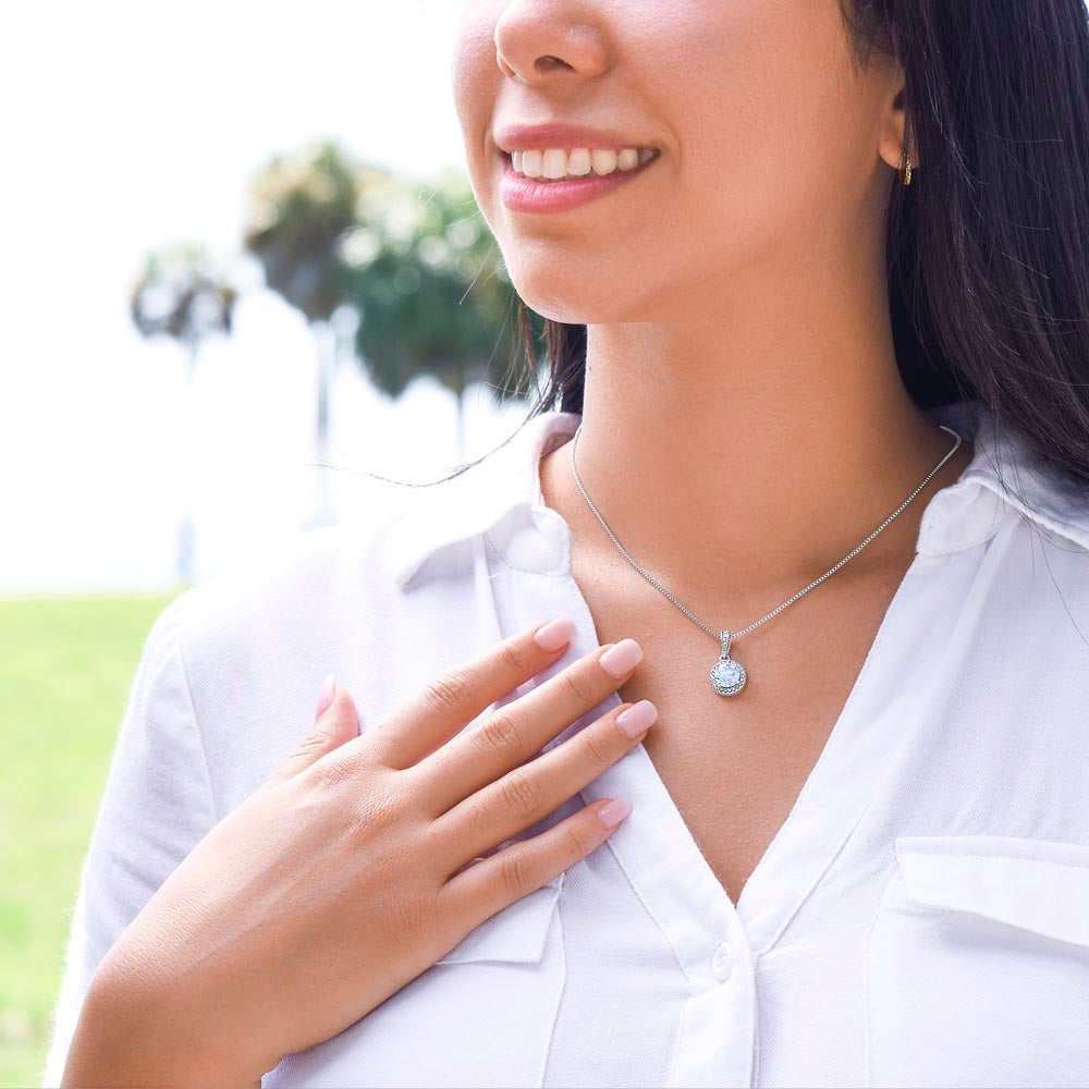 A diamond halo white gold necklace on a woman's neck with a white shirt outside