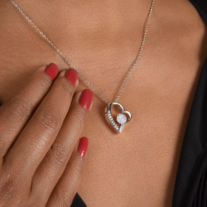 Heart-shaped necklace with a diamond pendant worn by a person with red nail polish.