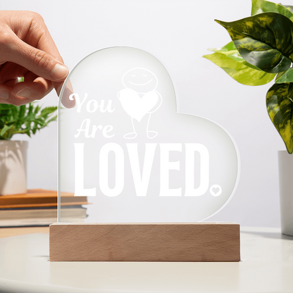 You are loved plaque with hand showing transparency against a white wall