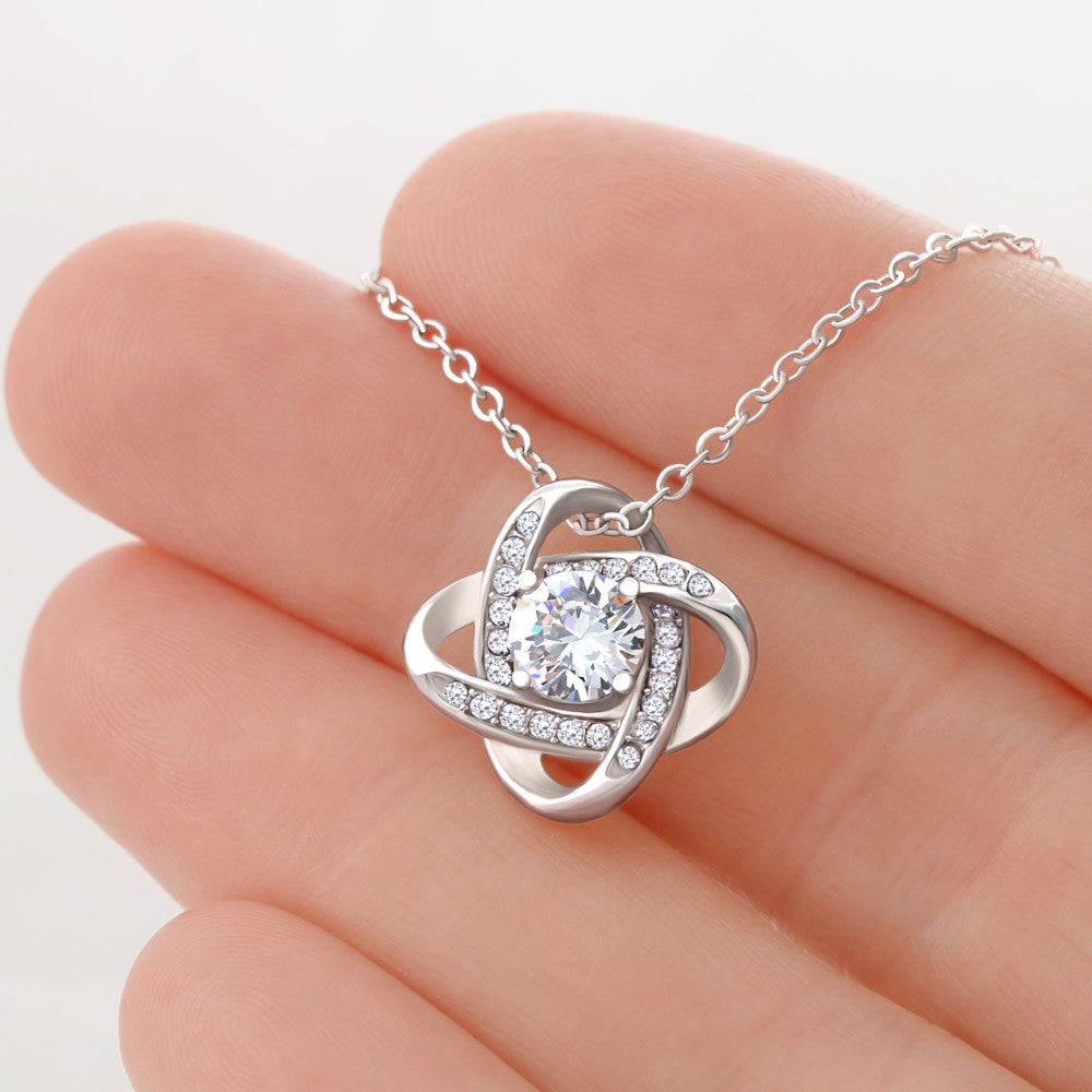 White gold knot necklace close up on fingers.